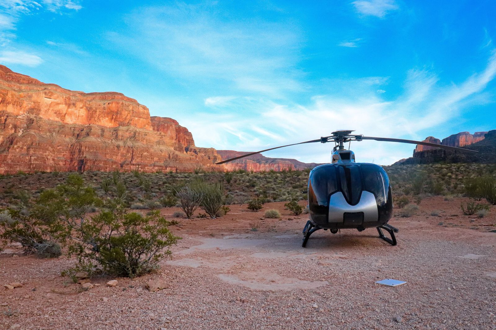 A helicopter parked on a red desert pad below Grand Canyon cliffs